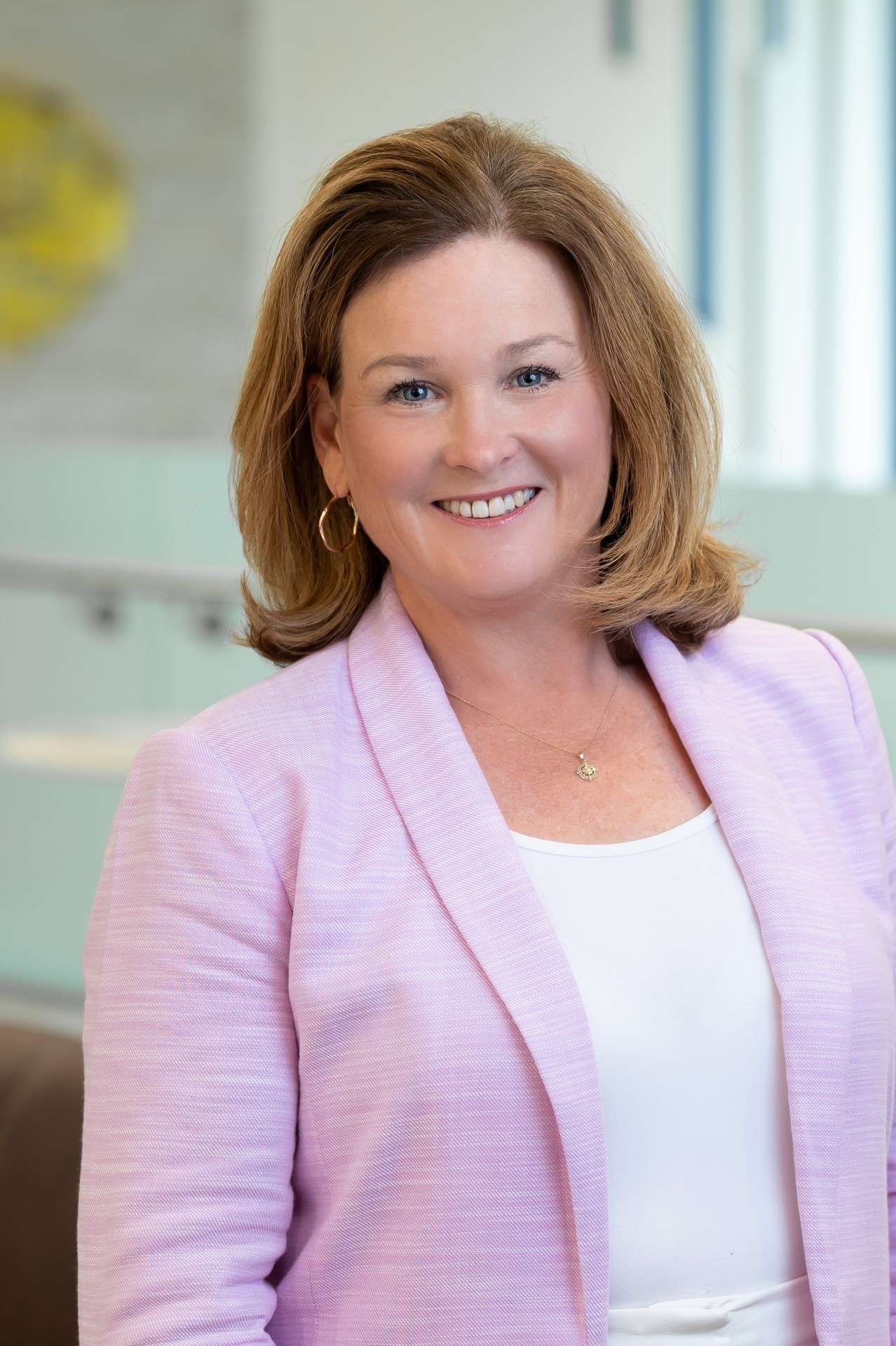 Keri Walker Pfeifer smiles, wearing a light purple jacket in a modern office setting.