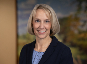 Headshot of Kirsten Andrews Woelper with a background of trees and soft colors.