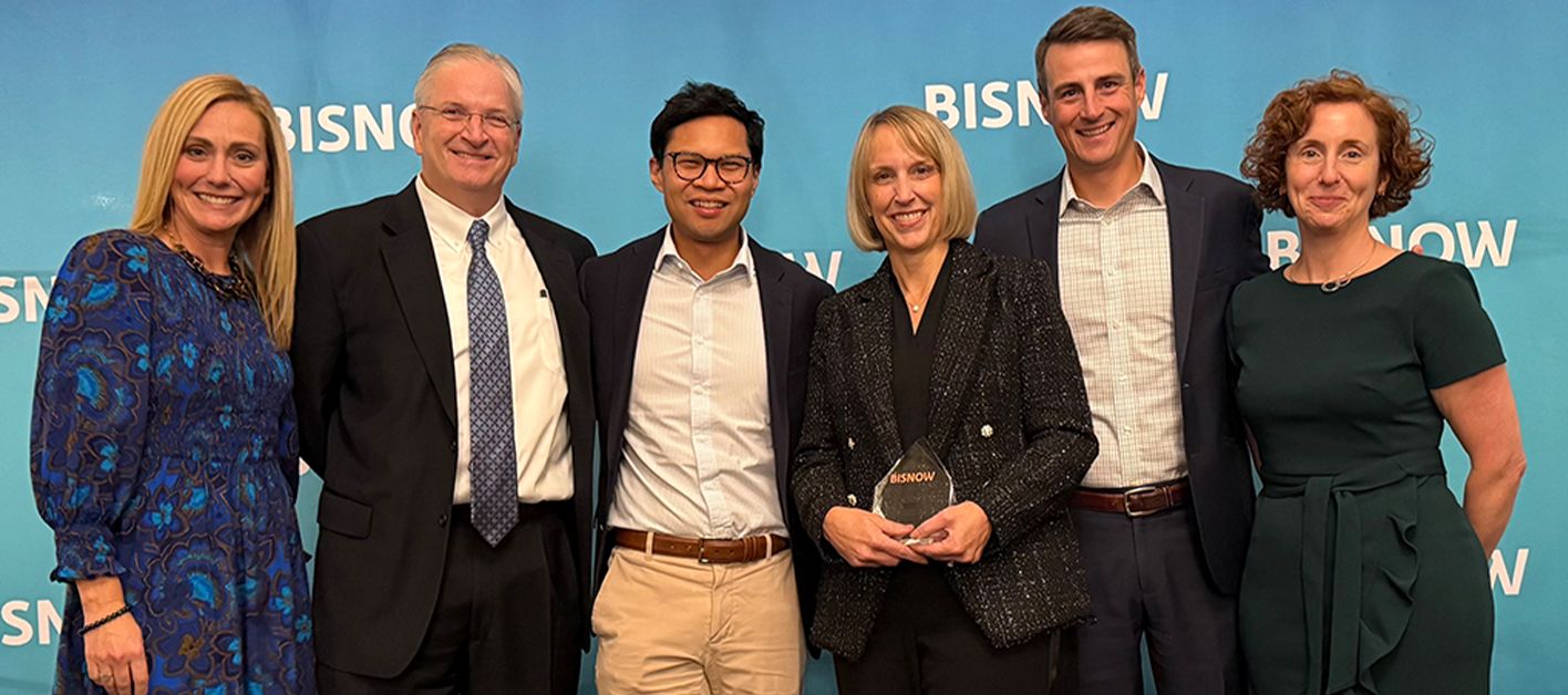 Group of six people posing together at an awards event with a blue background.
