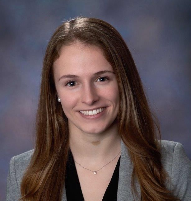 Headshot of a smiling young woman with long brown hair, wearing a blazer.