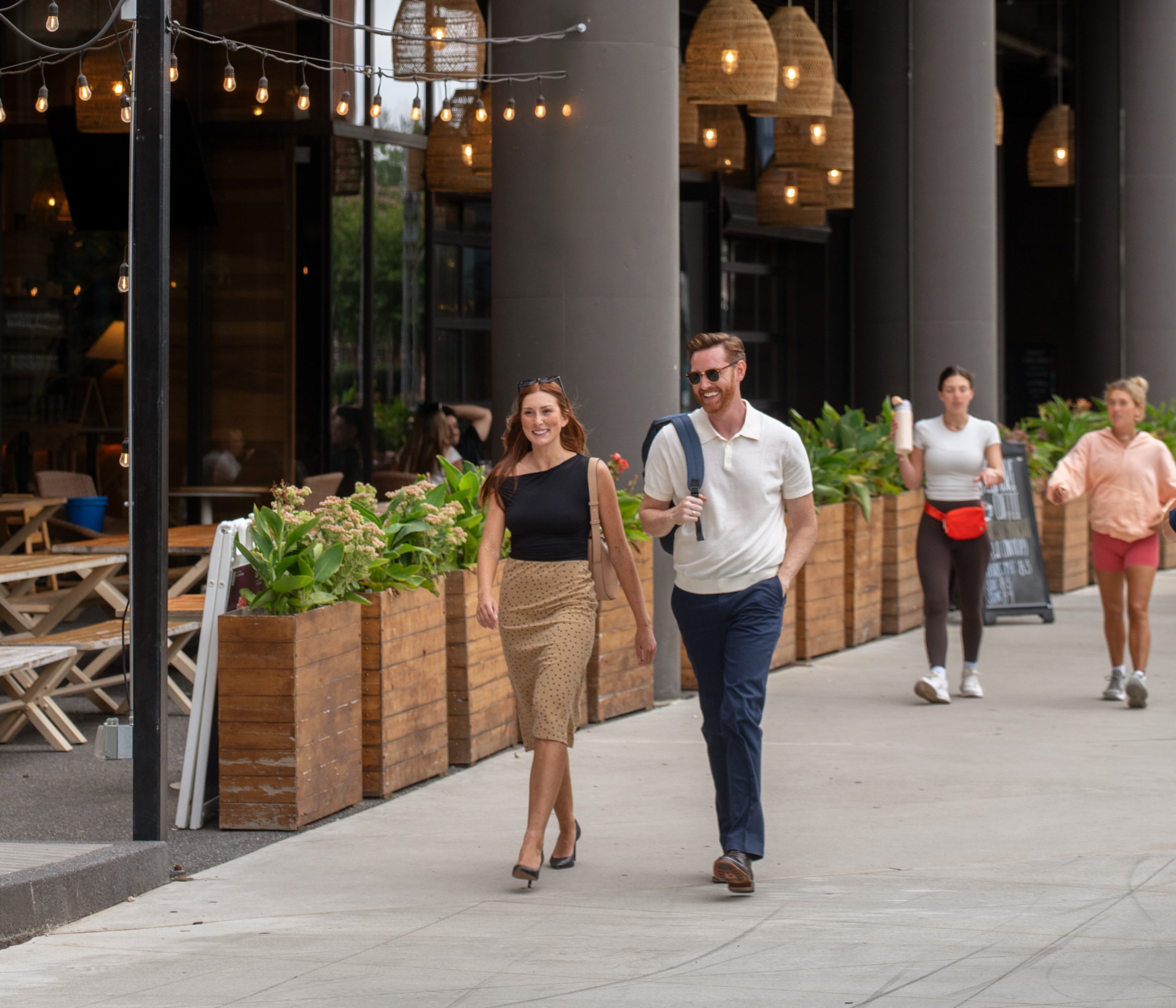 Couple walking along a street with outdoor dining and plants.