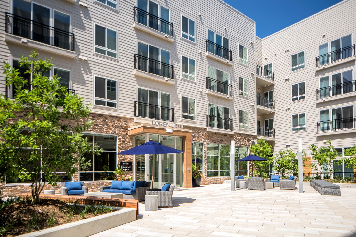 Modern apartment complex courtyard with lounge seating and umbrellas.