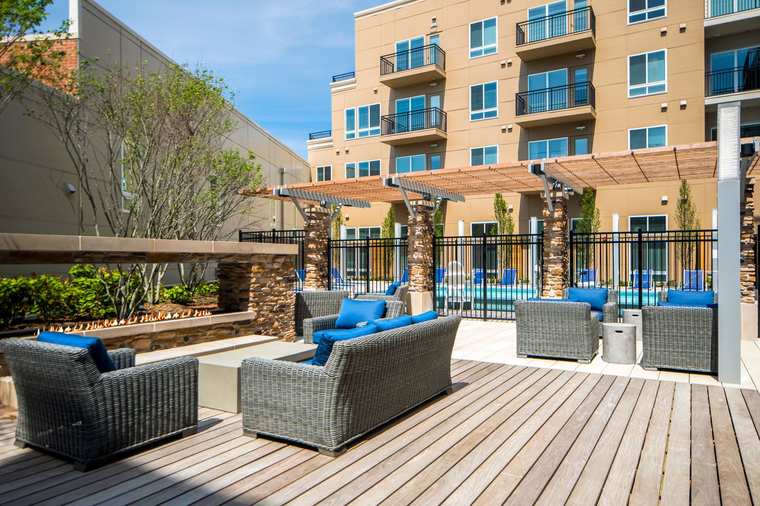 Outdoor lounge area with modern furniture by a pool, surrounded by trees and buildings.