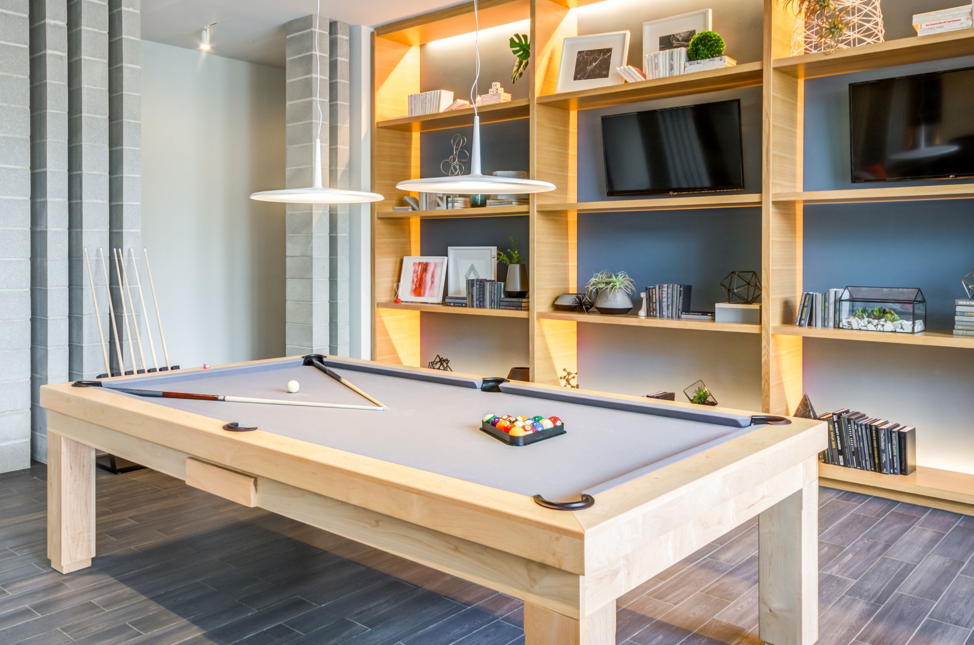 A modern game room featuring a pool table and wooden shelving with decor.