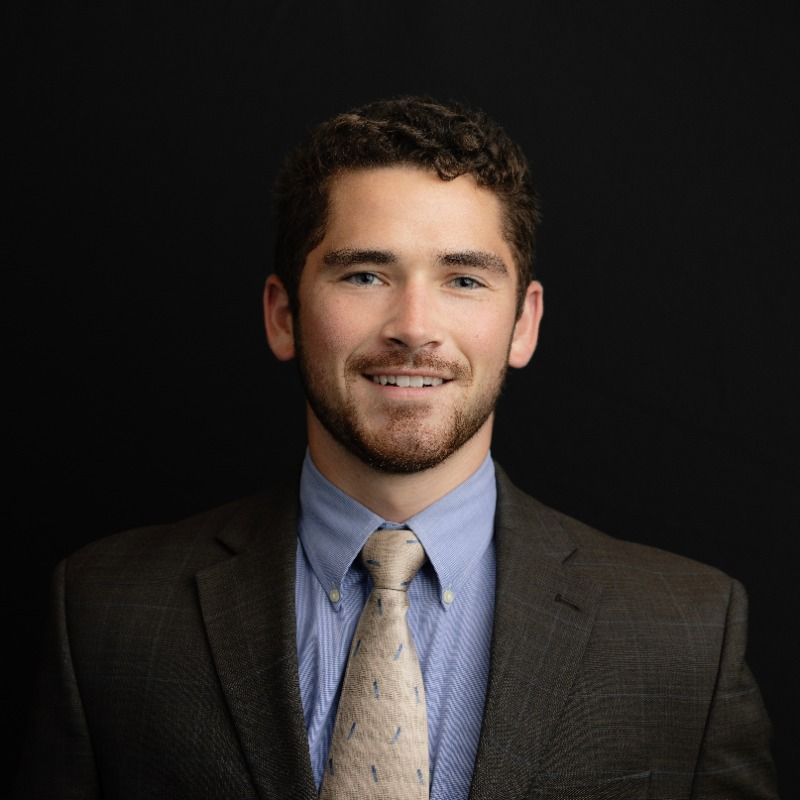 Smiling man in a suit and tie against a dark background.
