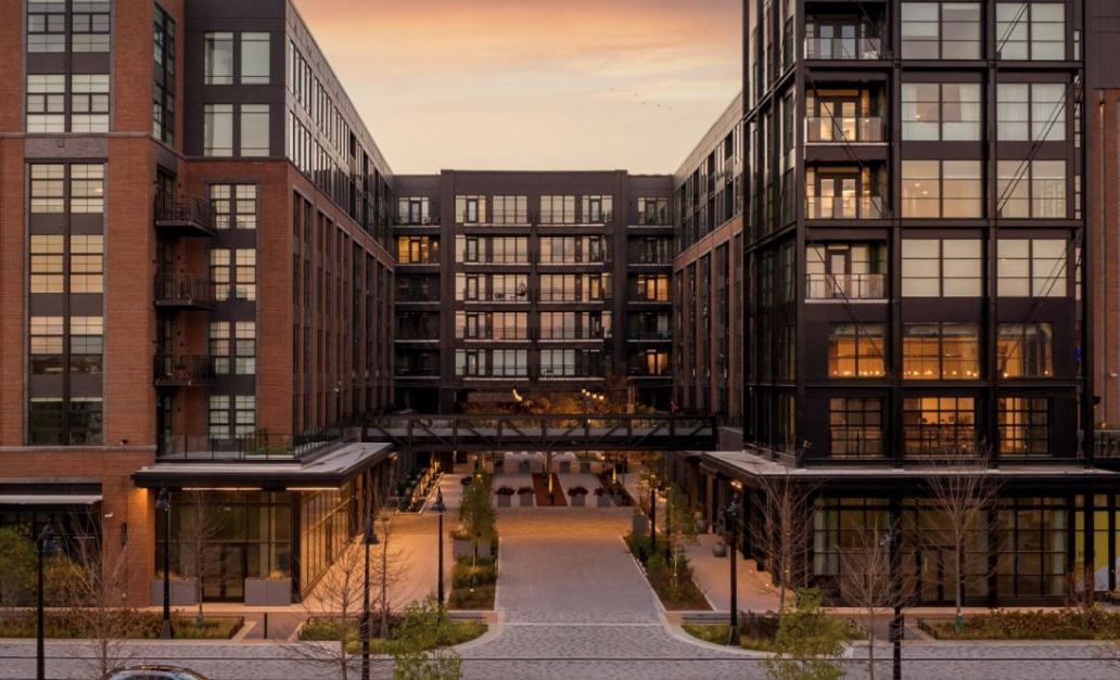 Modern brick apartment buildings at dusk with warm lights and a central courtyard.