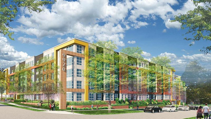Modern multi-story apartment building surrounded by greenery under a cloudy sky.