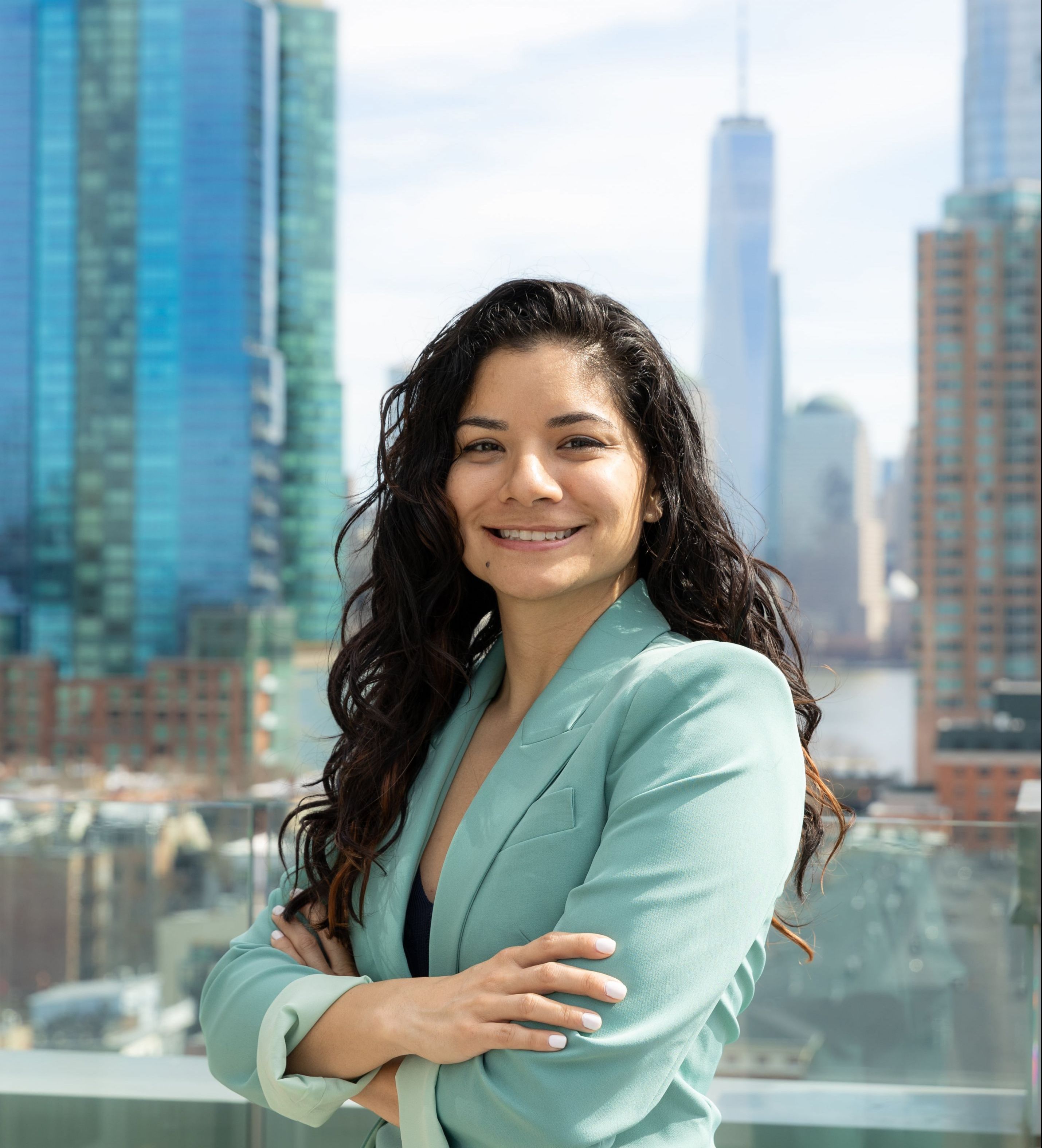 Person with curly hair smiling in front of city skyline and tall buildings.