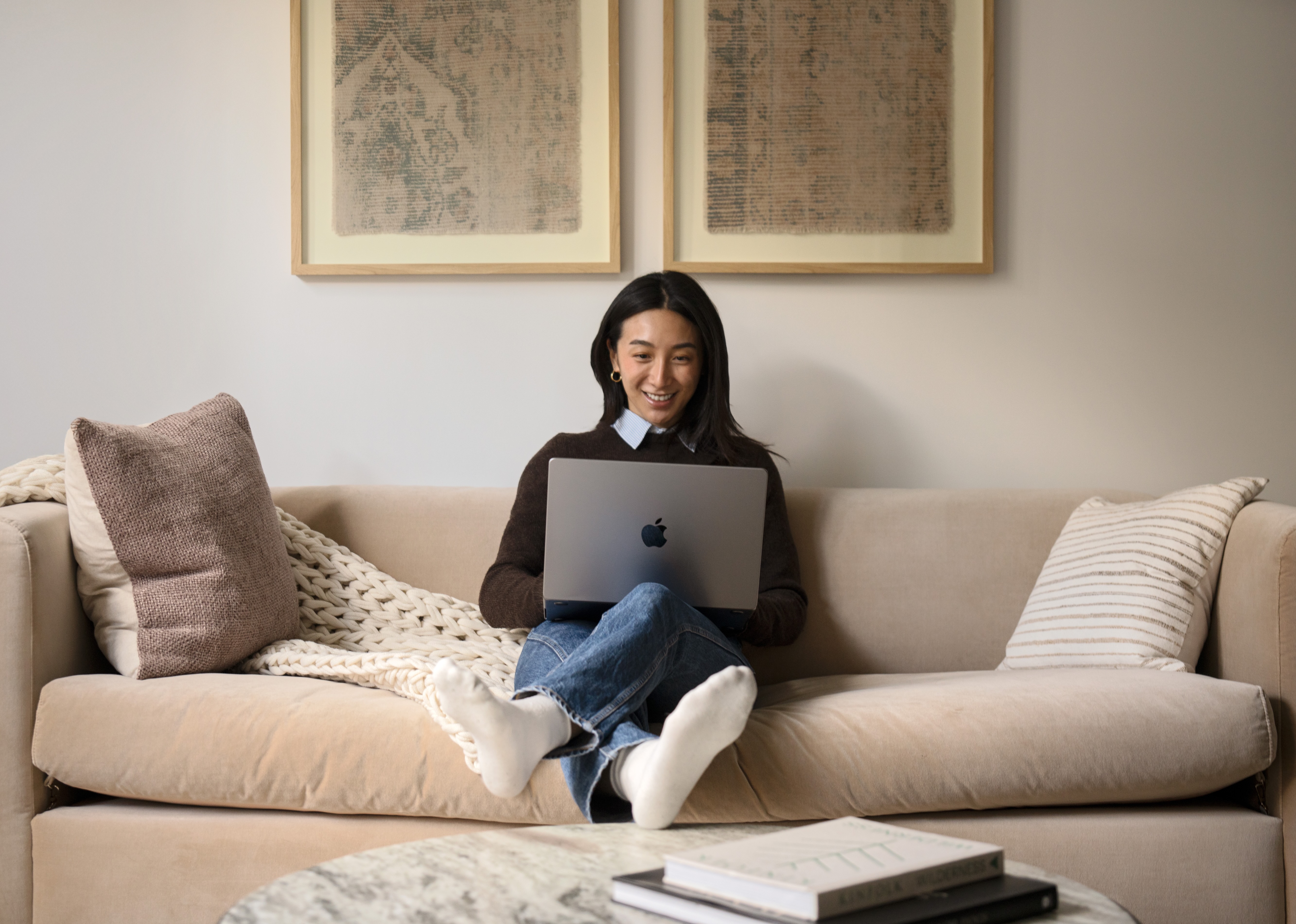 A young woman sitting on a sofa using a laptop with a cheerful expression.