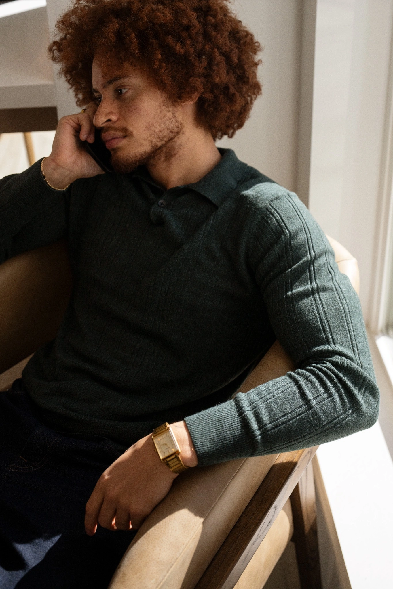 Man with curly hair in a green sweater talking on the phone.