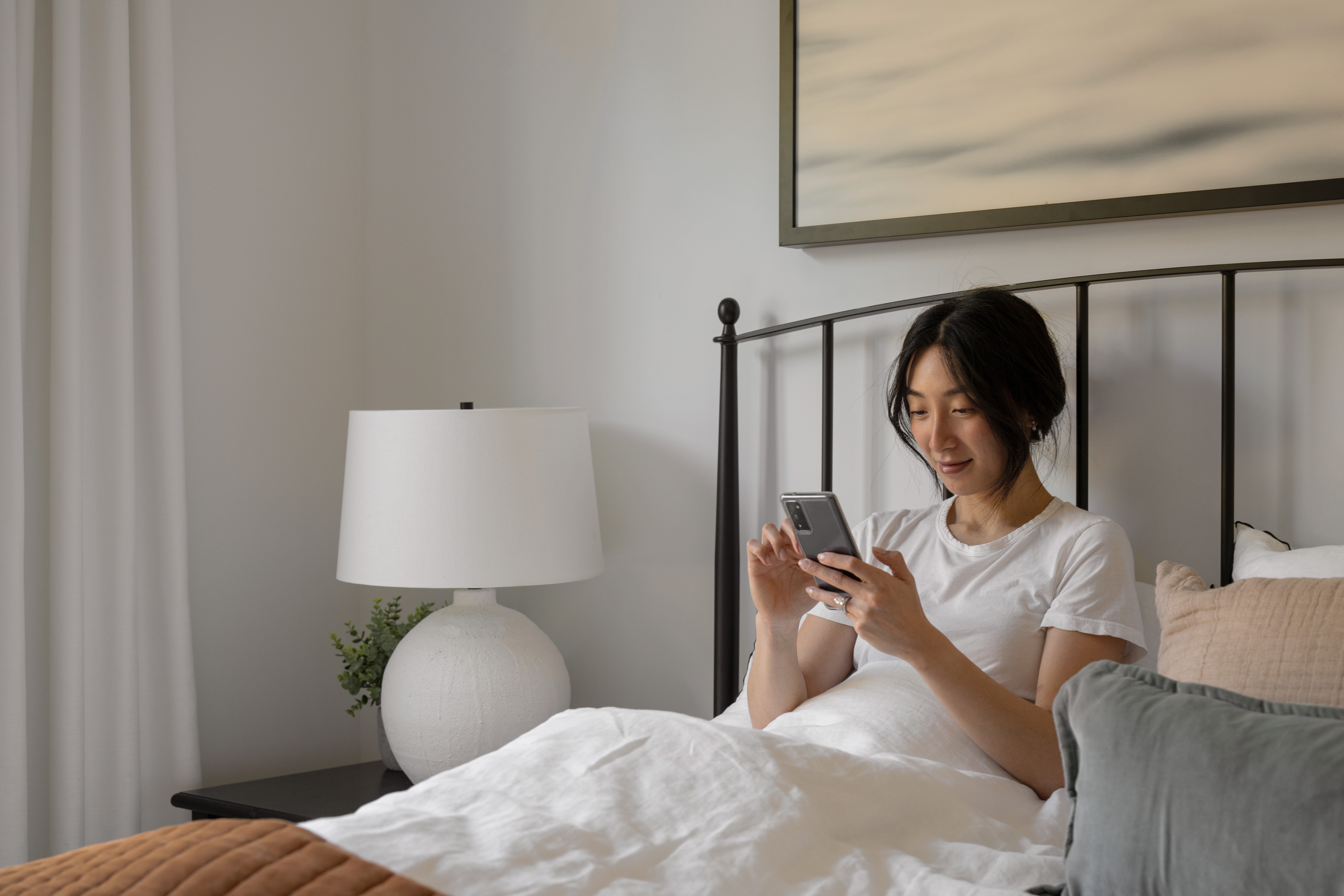 Person sitting in bed using a smartphone with a lamp beside them.
