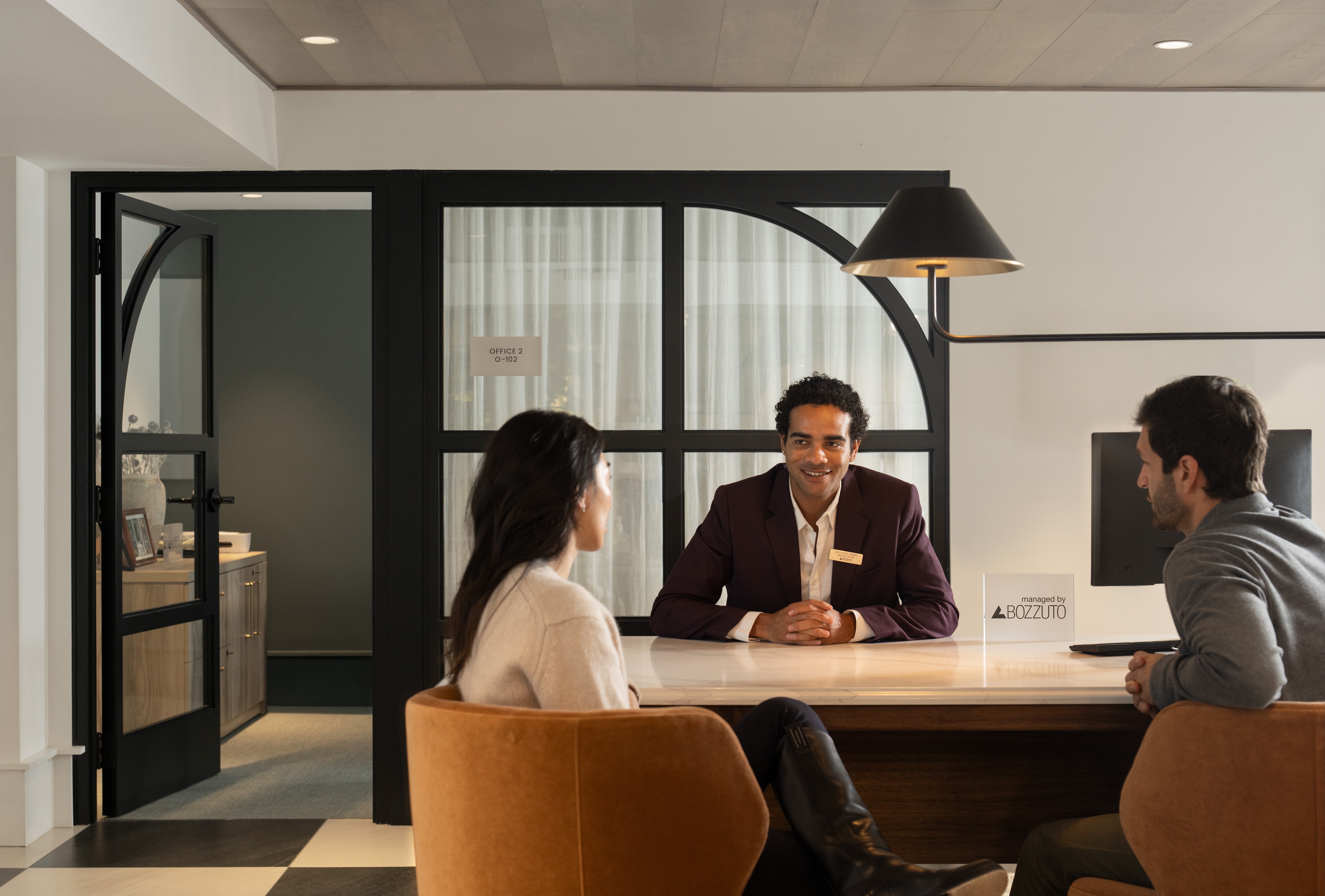 A hotel receptionist assisting two guests at a modern front desk.