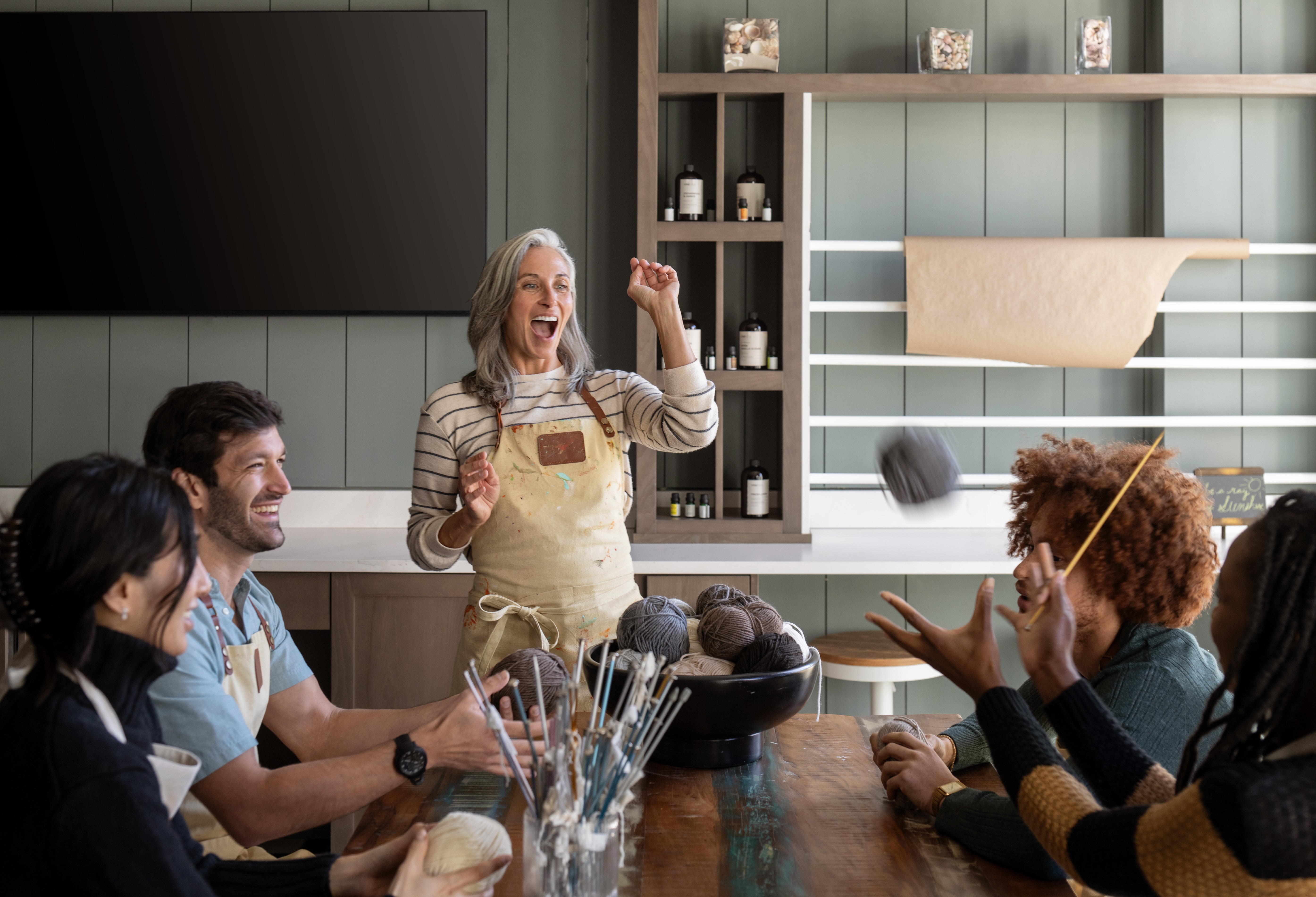 A group of people gathered around a table watching a woman enthusiastically speak.