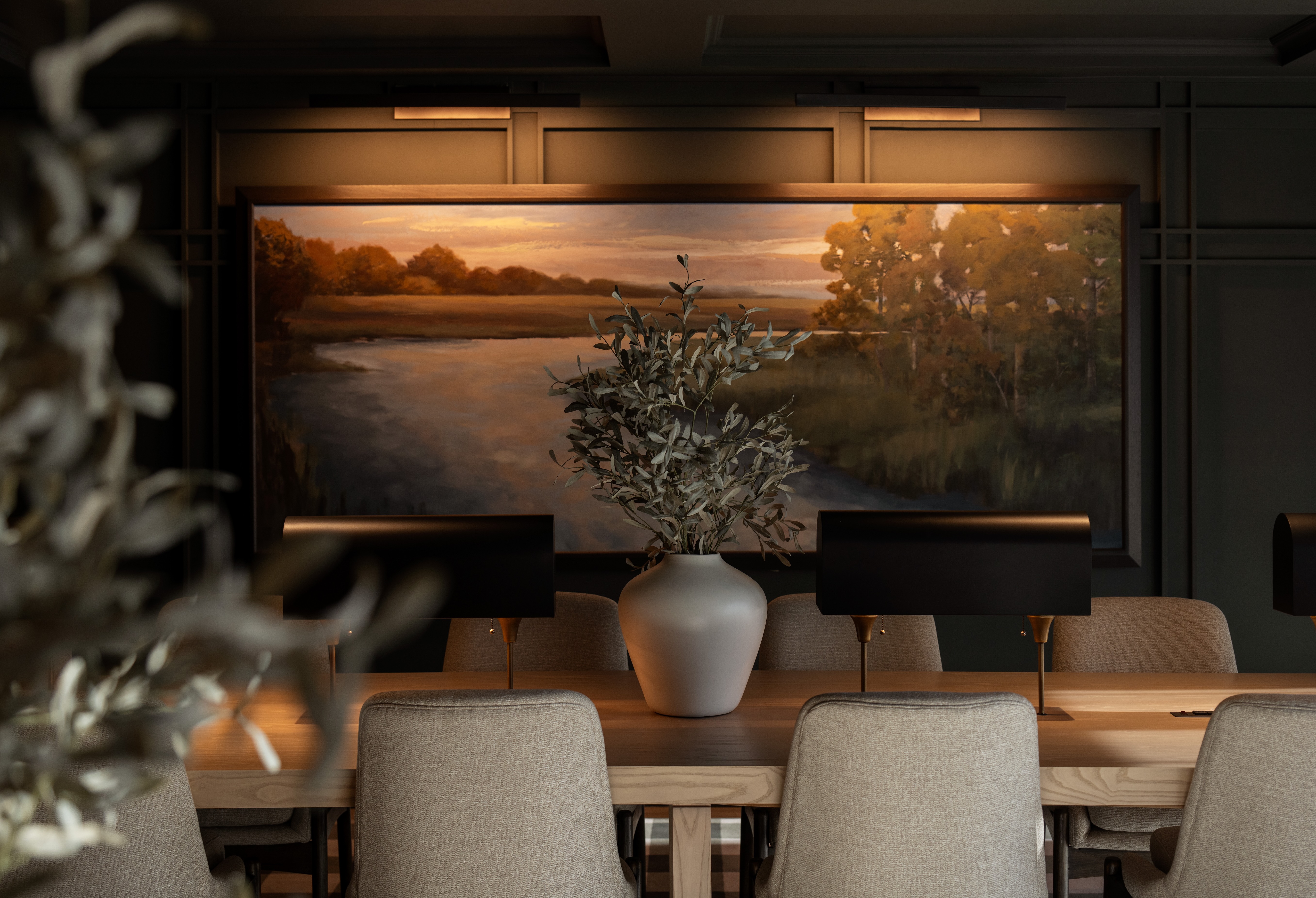 Elegant dining area with a large landscape painting and a central vase.