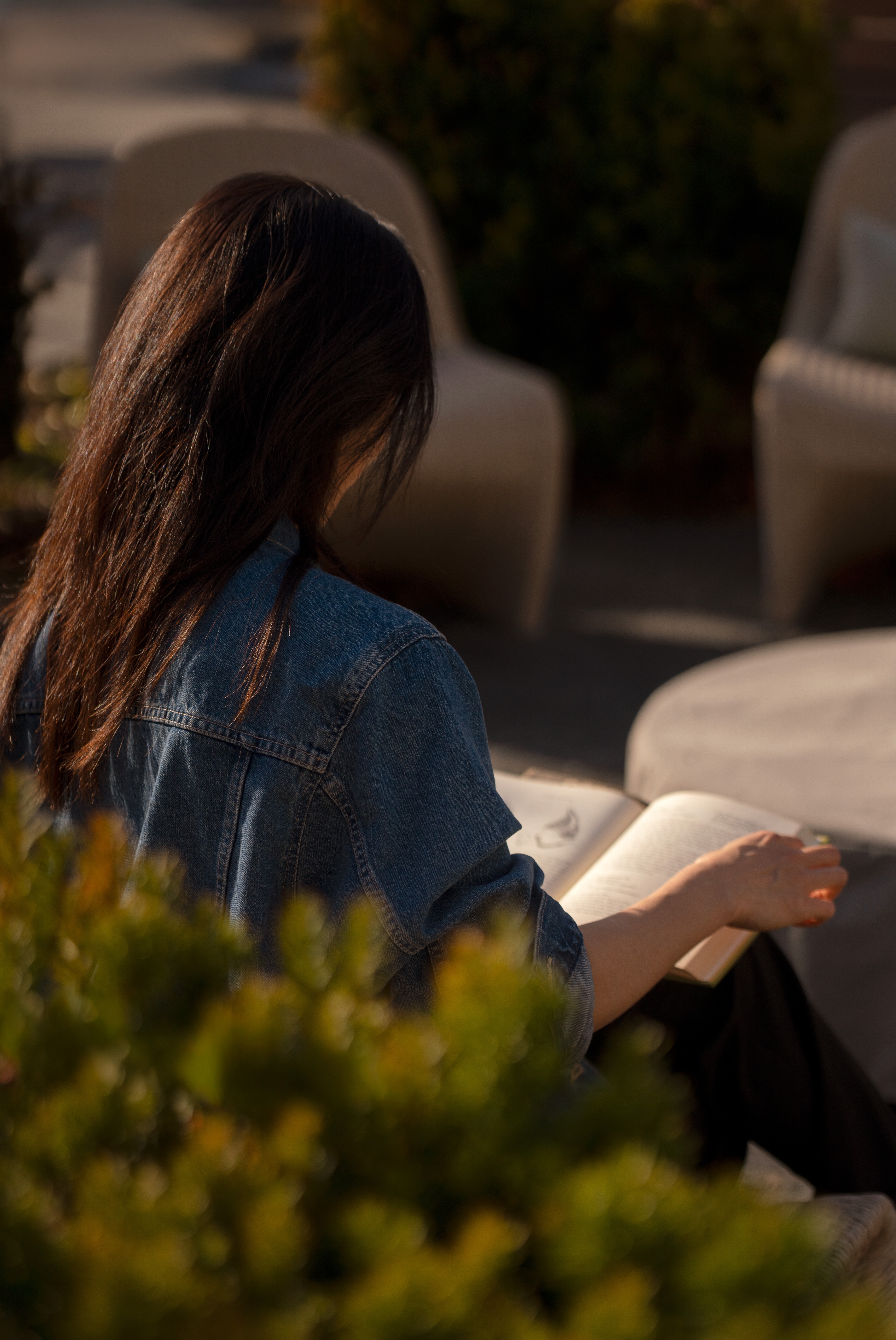 Person reading a book in a garden setting with blurred plants.