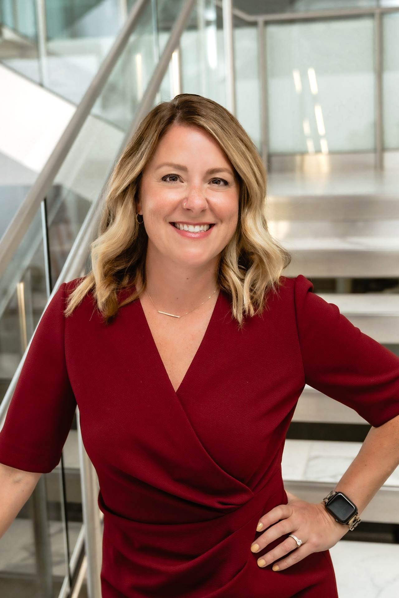 Stephanie Rath, smiling, stands confidently on a staircase in a modern interior setting.