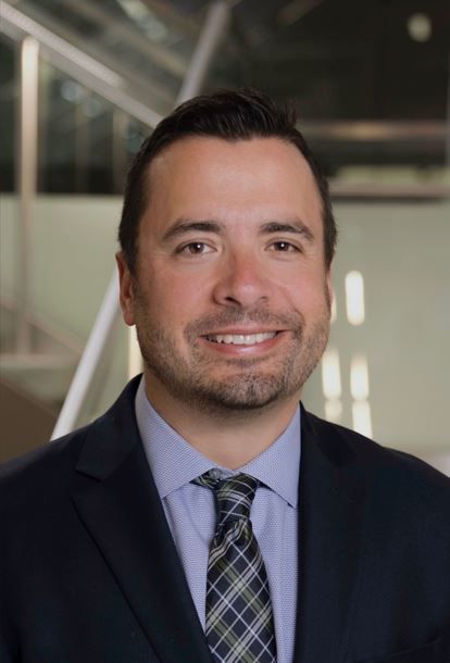 Professional man smiling in a suit with a modern building backdrop.