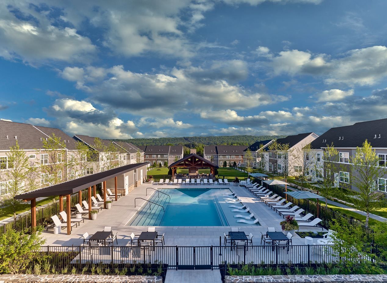 Modern apartment complex with a swimming pool and lounge area under a partly cloudy sky.