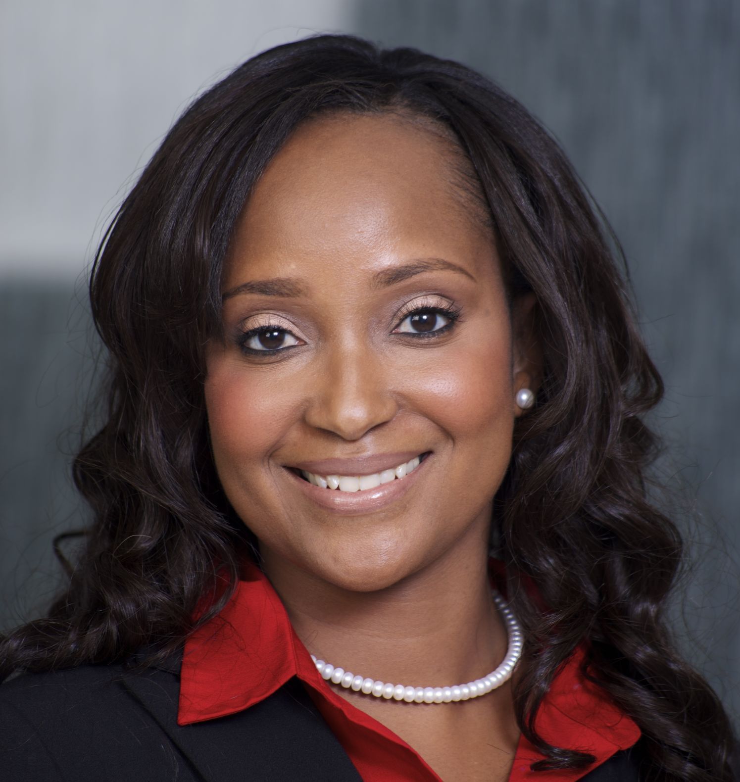 Smiling woman with long, wavy hair wearing a red blouse and pearls.