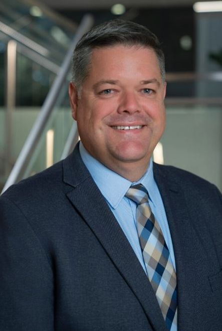 Professional man in a suit, smiling, with a modern office background.