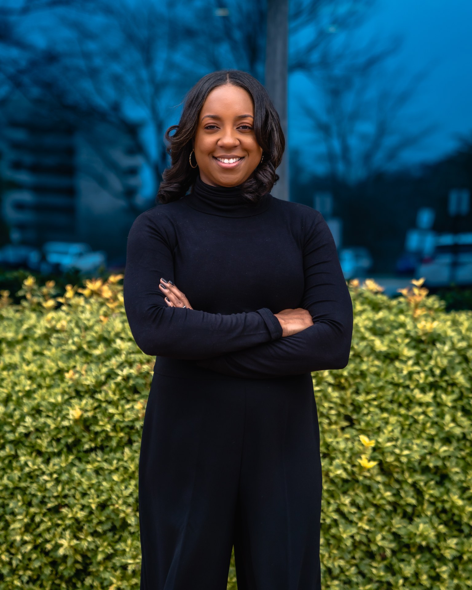 Shawaun Alexander stands confidently with arms crossed in front of greenery and a blue backdrop.