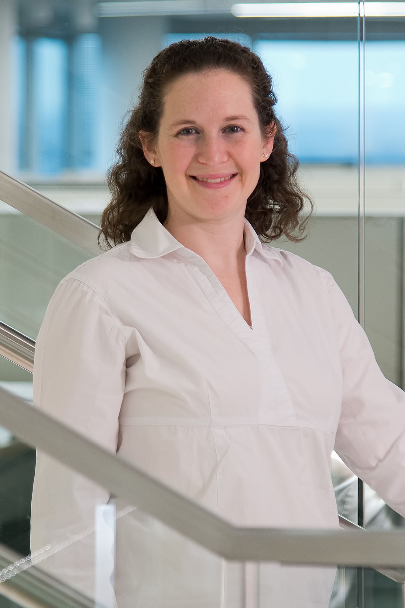 Smiling woman in a light-colored shirt stands by a modern staircase.