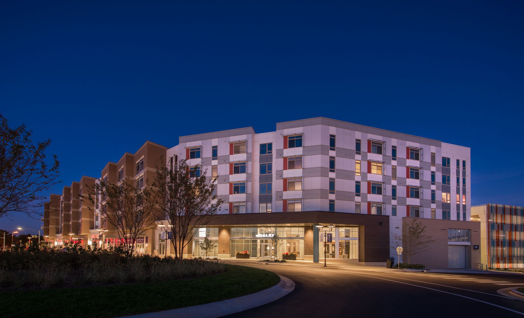 Modern hotel building at dusk with illuminated windows and landscaped surroundings.