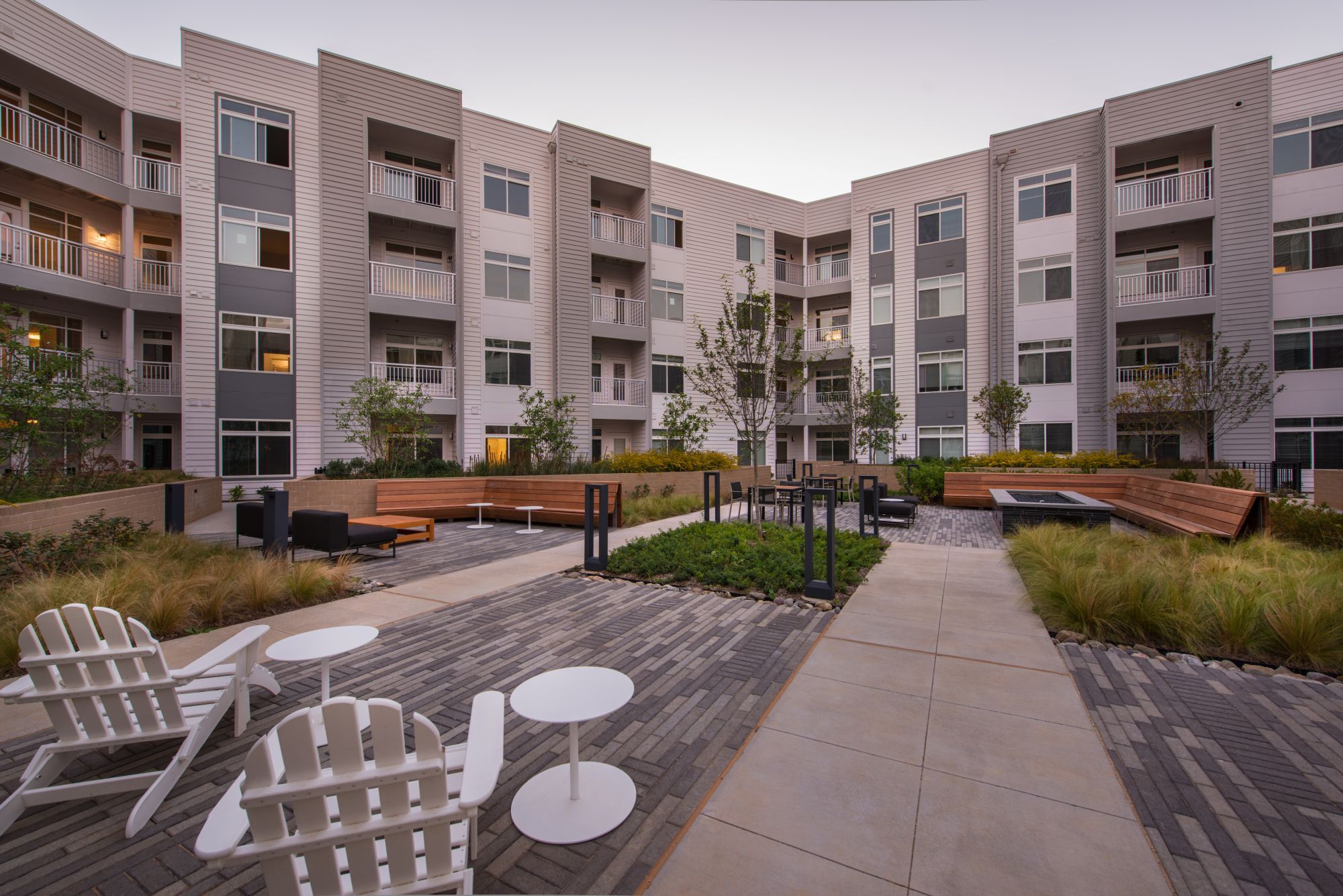 Modern apartment complex courtyard with seating and greenery.