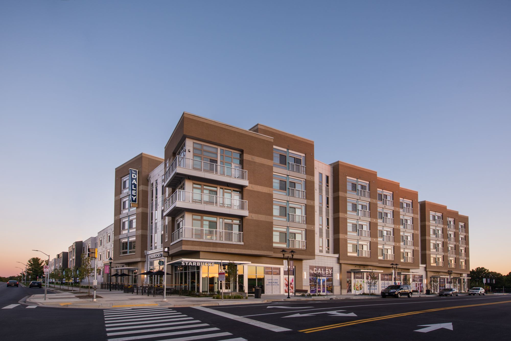 Modern multi-story building with retail on the ground floor at sunset.