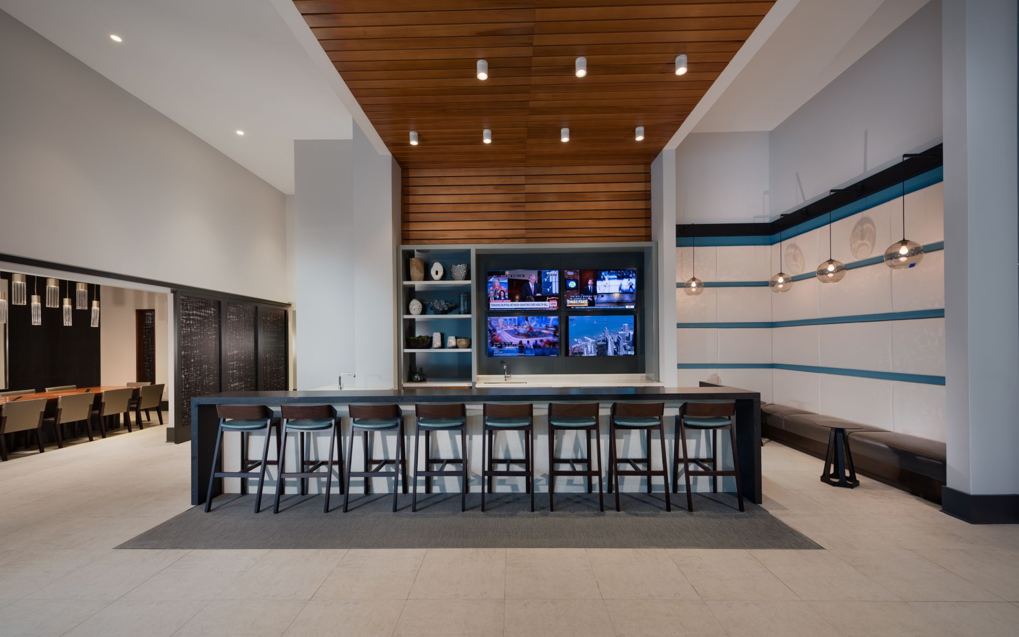 Modern bar area with wooden accents and multiple screens, featuring tall stools and minimal decor.