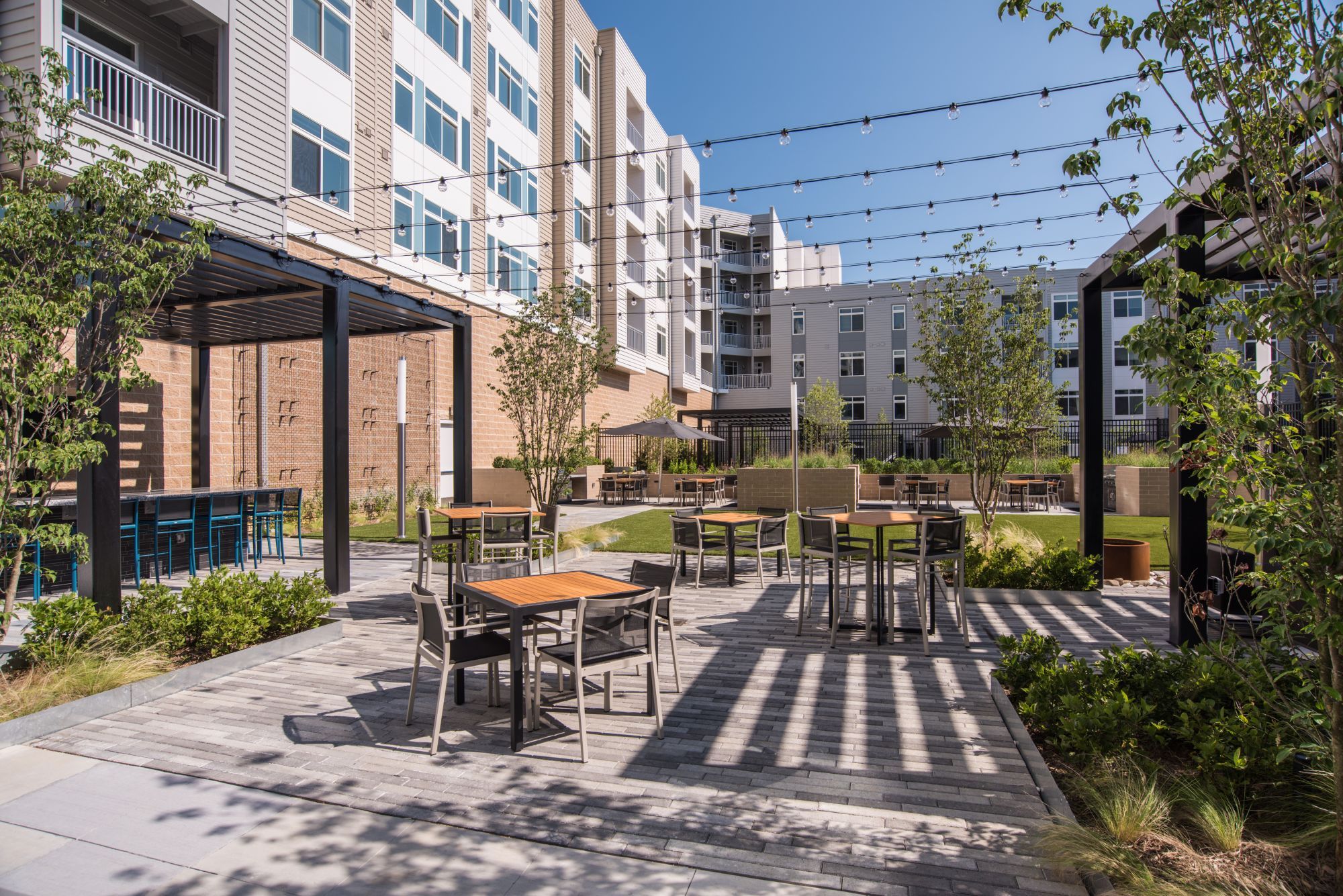 Modern outdoor courtyard with seating, greenery, and string lights.