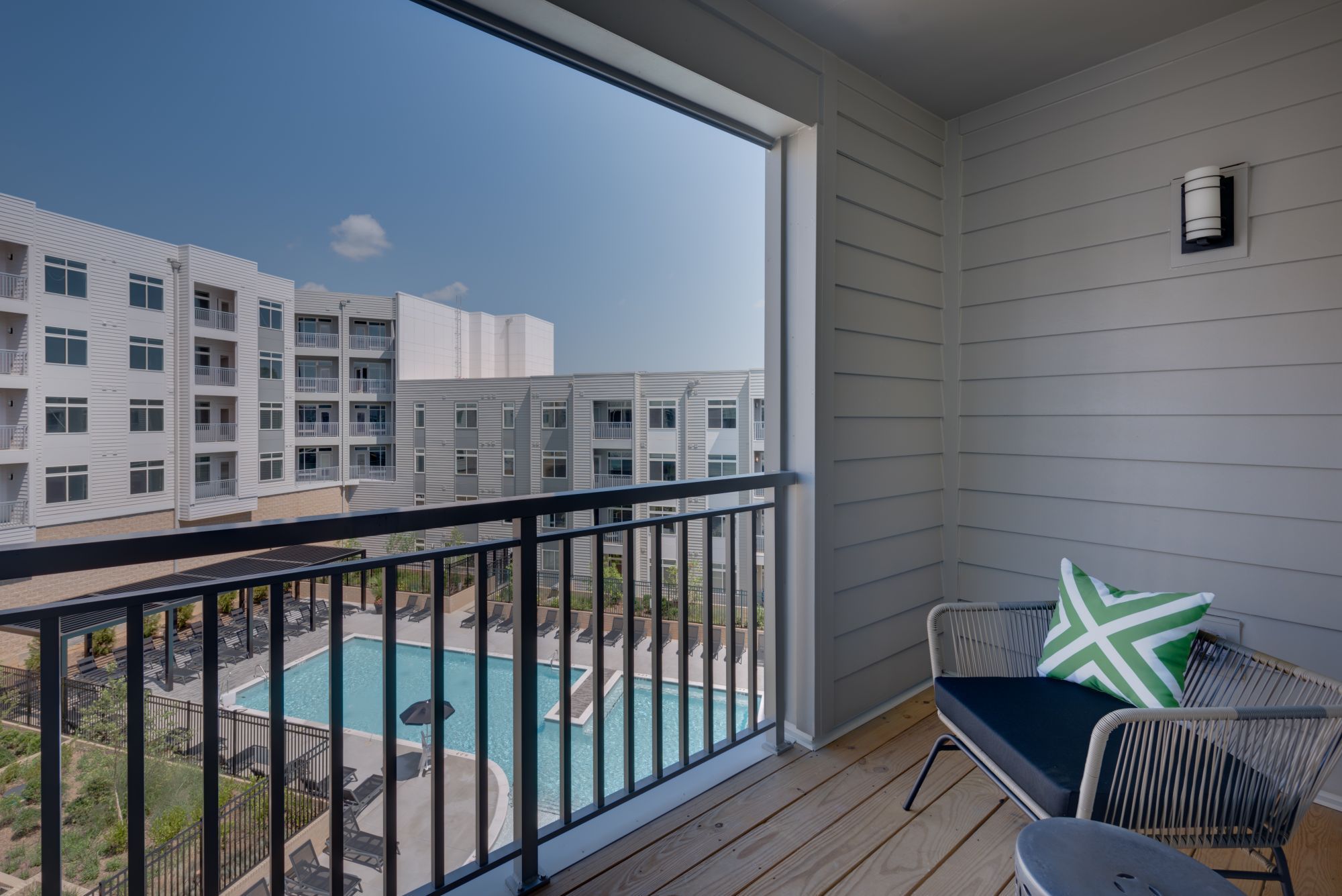 View from a balcony overlooking a pool and modern apartment buildings.