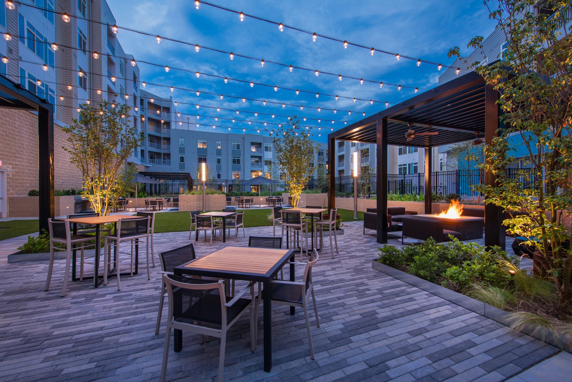 Outdoor patio with string lights, dining tables, and a fire pit at twilight.