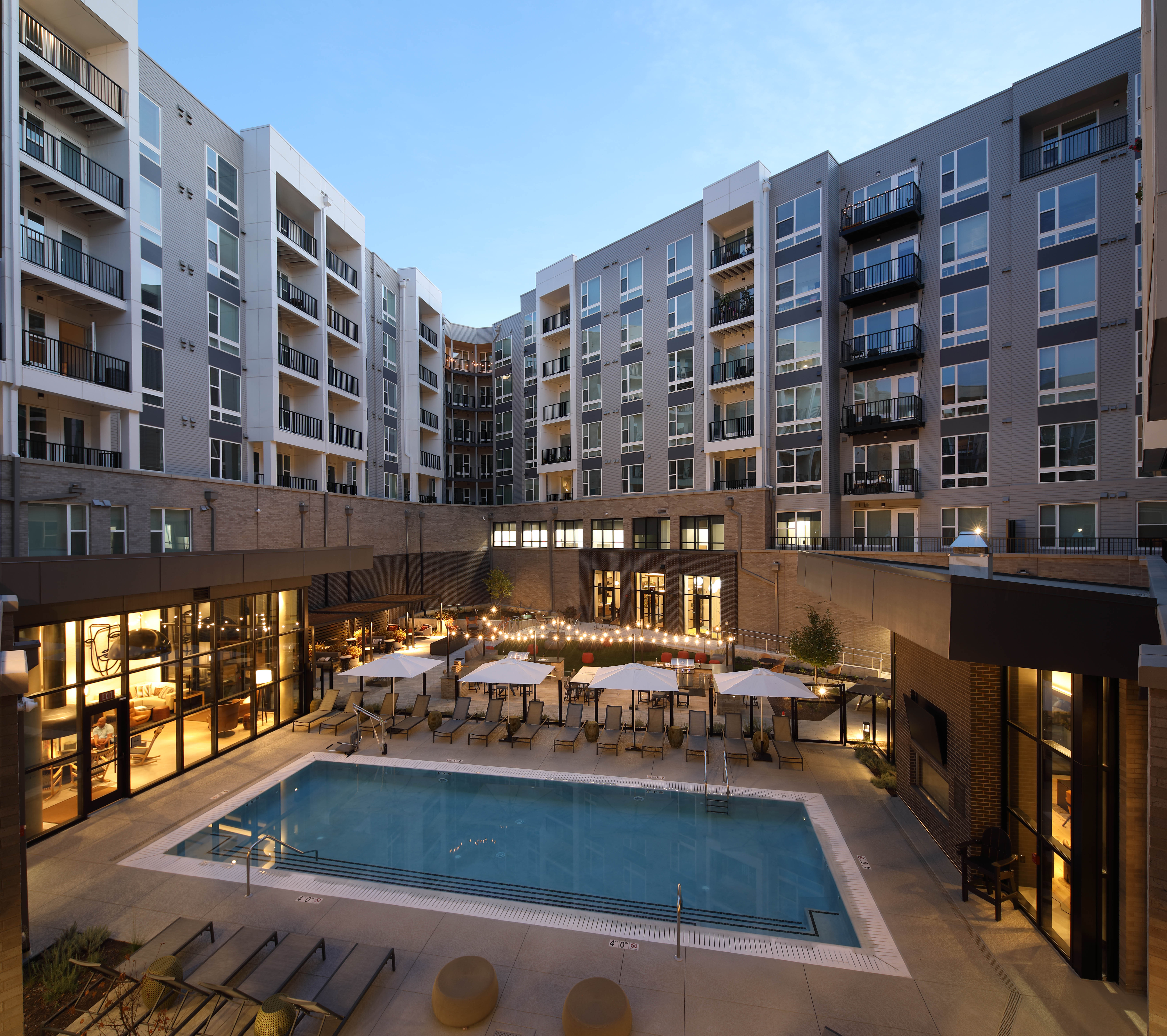 Modern apartment complex with a pool and lounge area at sunset.