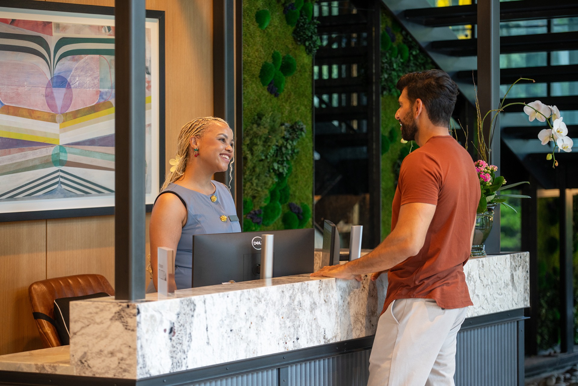 A receptionist smiles at a visitor at a modern front desk.