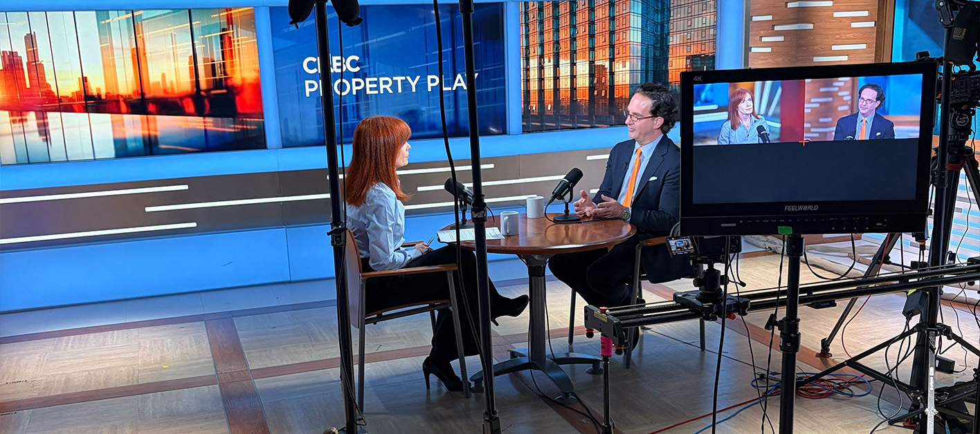 Two people speaking in a studio with a city backdrop and cameras set up.