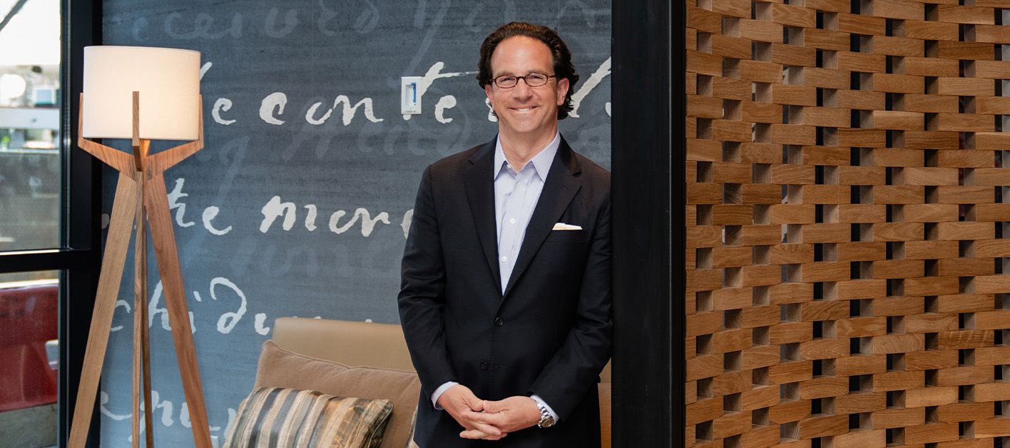 Man in a suit standing beside a modern lamp in a stylish interior setting.