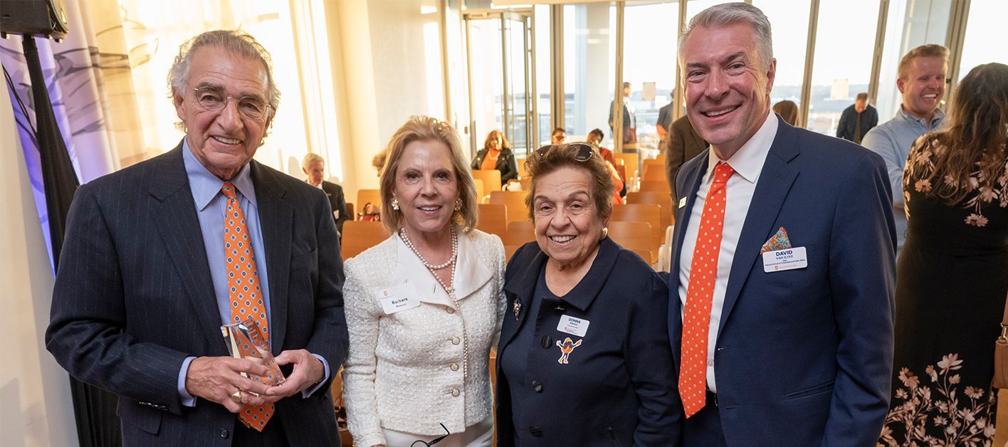 Four people pose together at an event, smiling with a bright, elegant background.