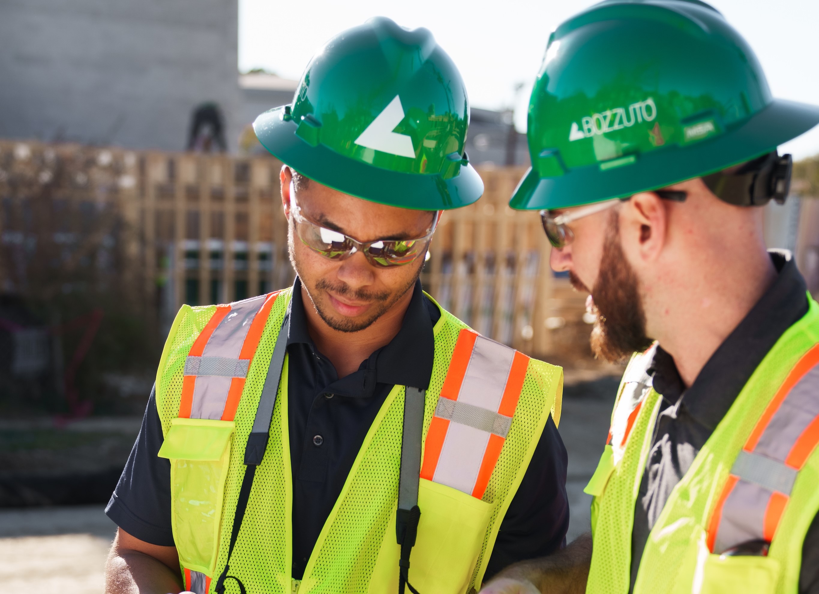 Two construction workers wearing safety gear review information on a tablet at a jobsite.