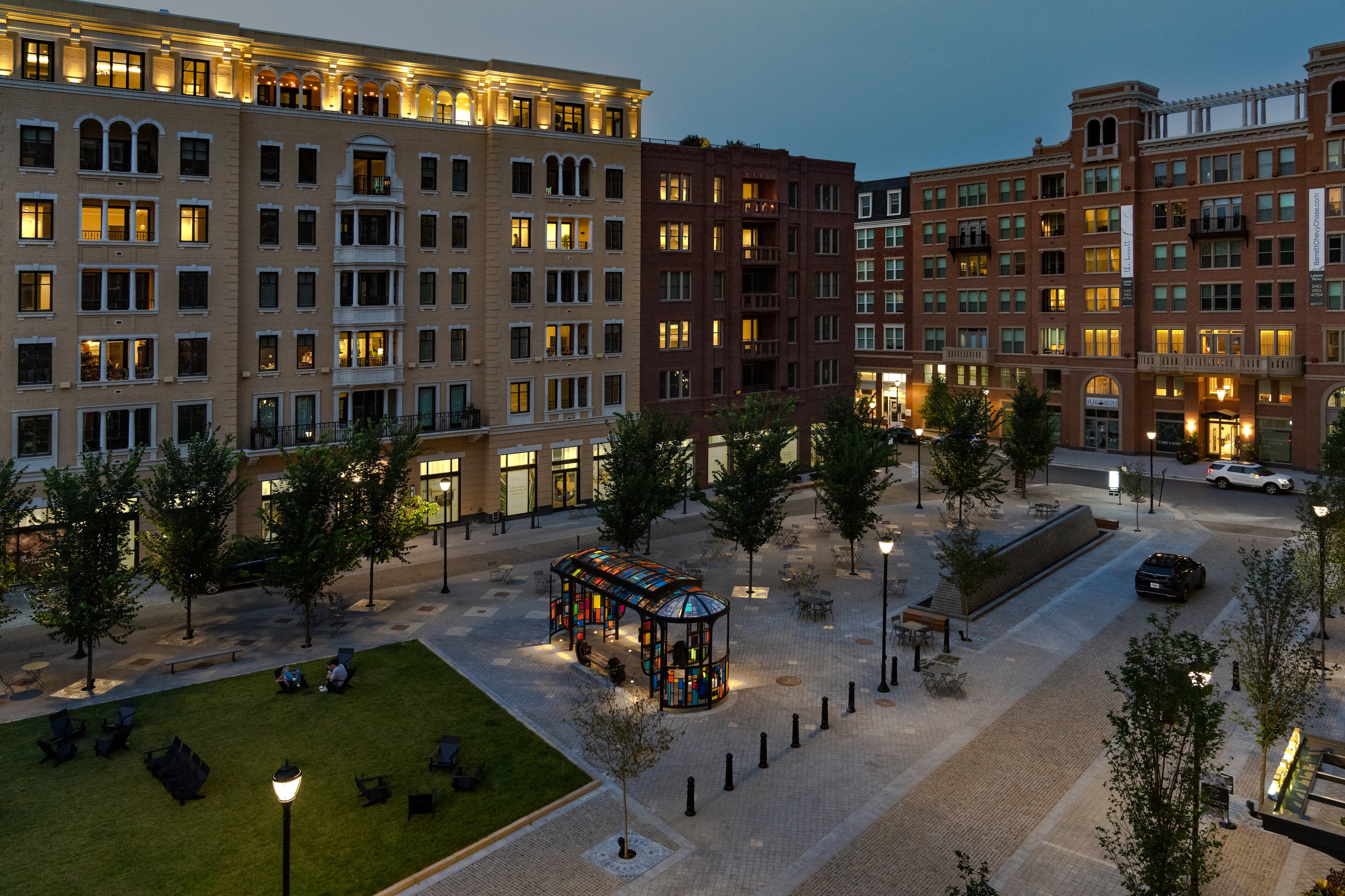 Urban plaza with modern buildings, trees, and streetlights at dusk.