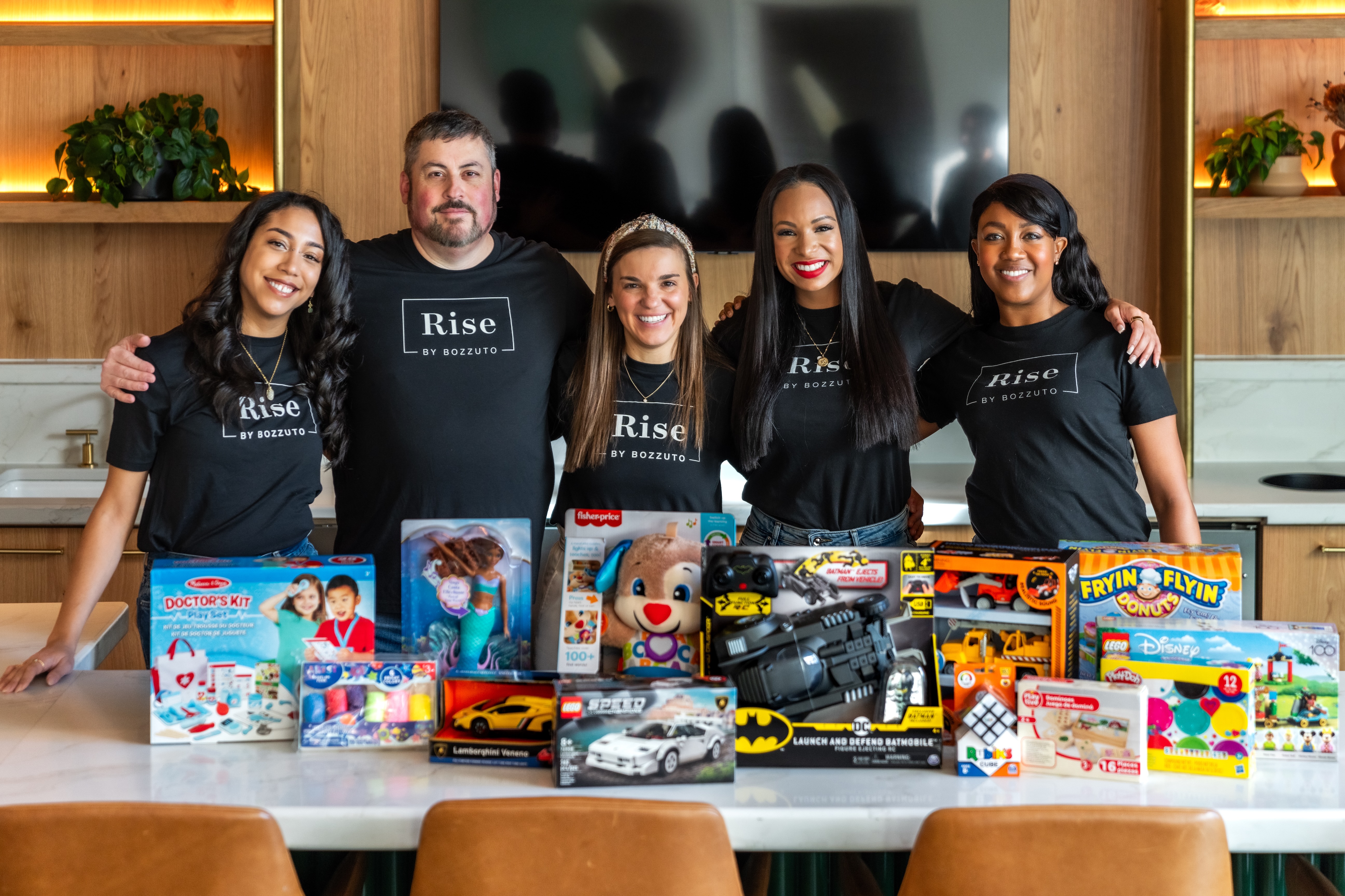 Five people in black shirts stand behind a table with various toys.