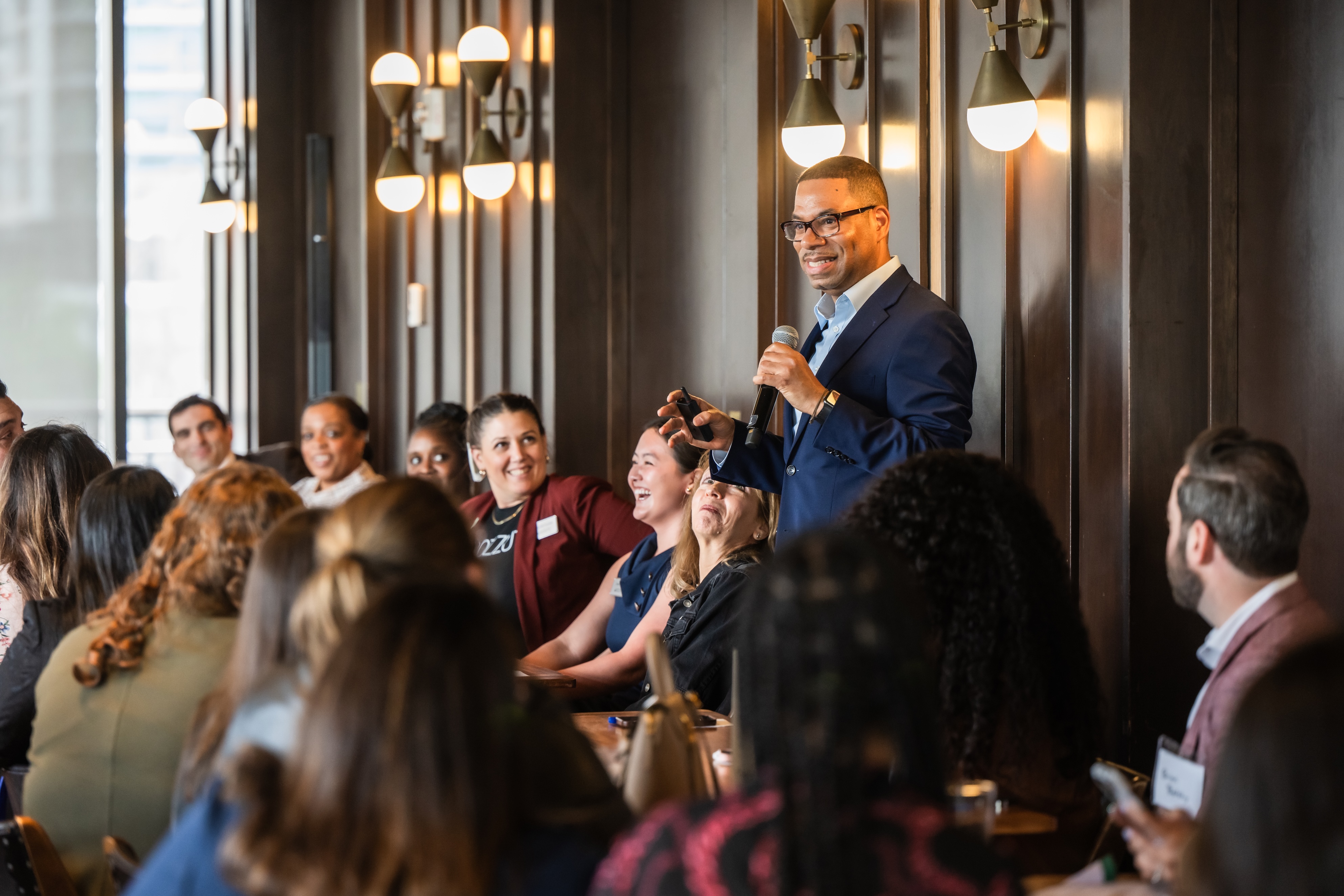 Speaker addresses an engaged audience in a modern indoor setting.