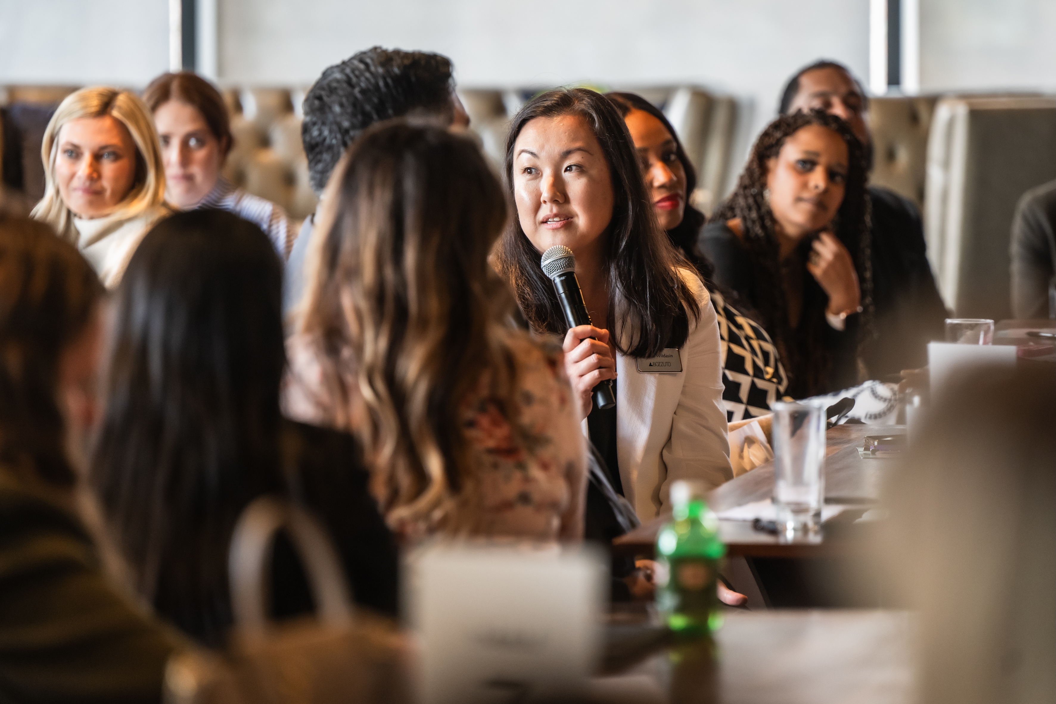 A woman speaking into a microphone at a panel discussion with audience members.