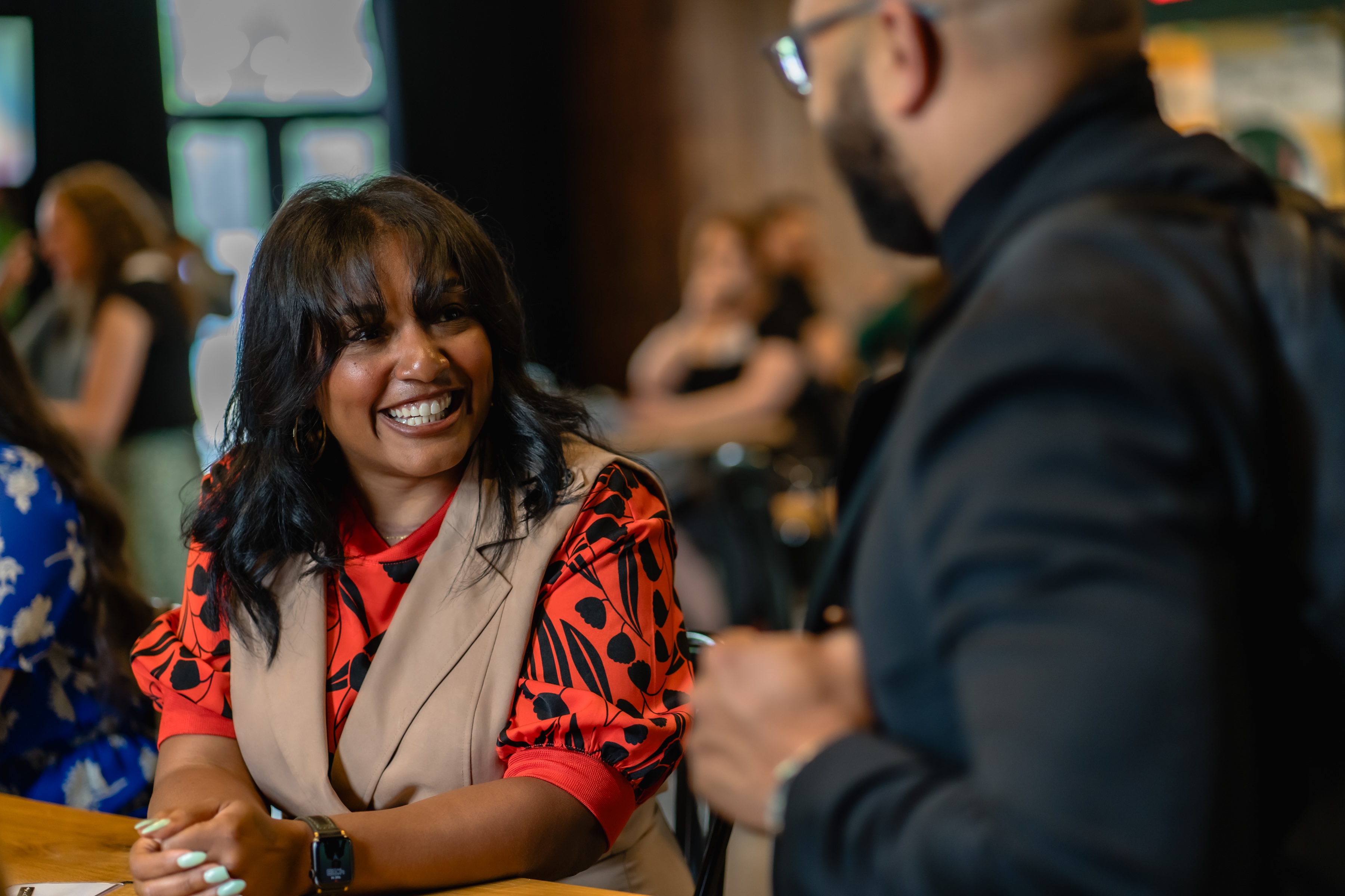 Smiling woman in a colorful shirt talks to a man at a social gathering.