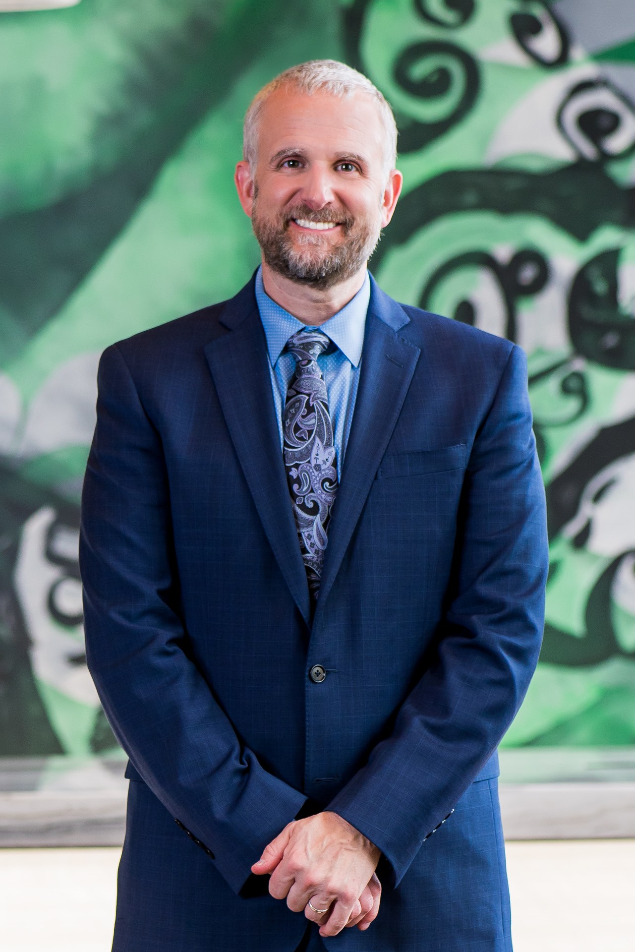 A smiling professional in a suit stands in front of green artwork, representing a Bozzuto Partner.