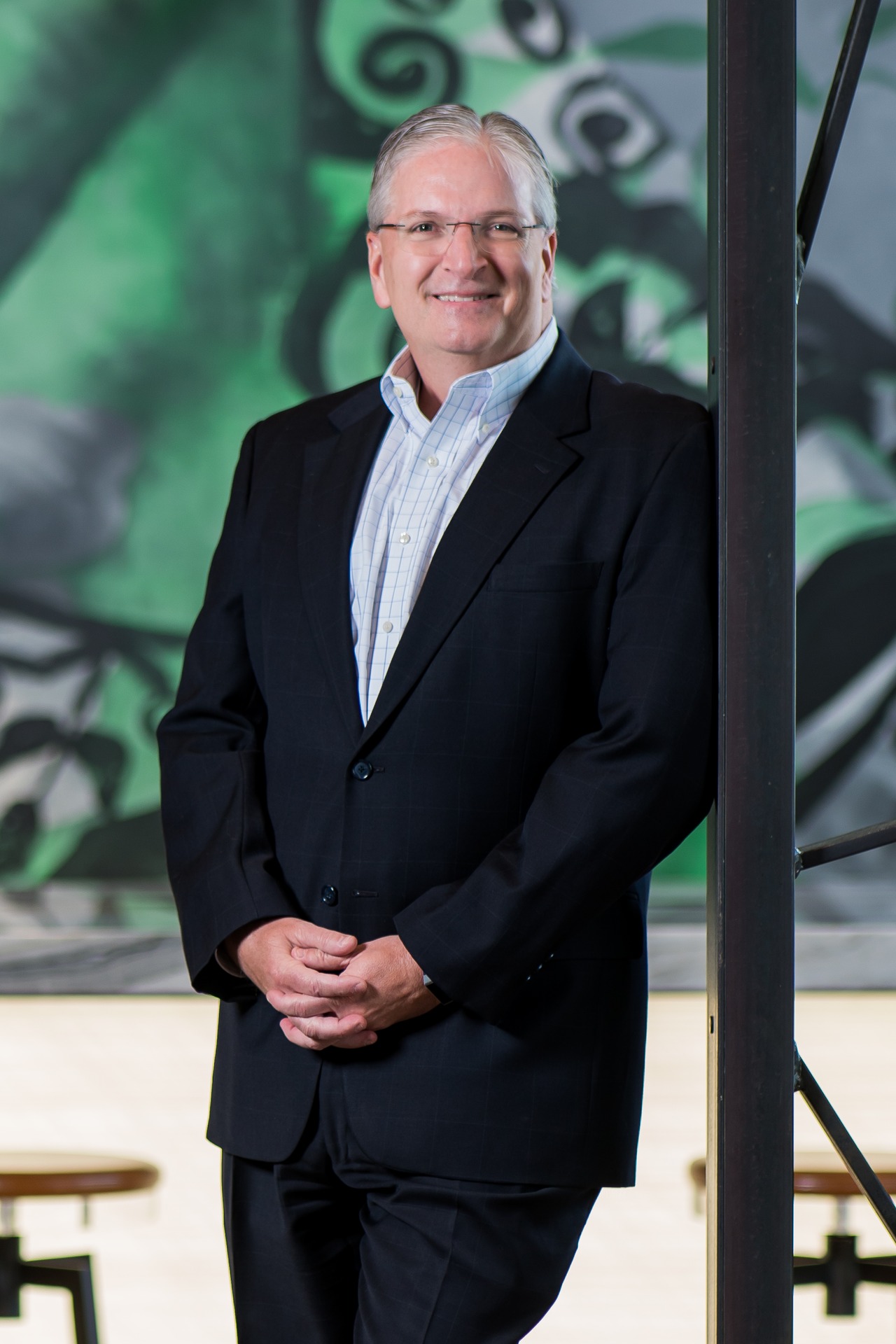 Daniel C. Murphy stands smiling in a suit against a vibrant mural background.
