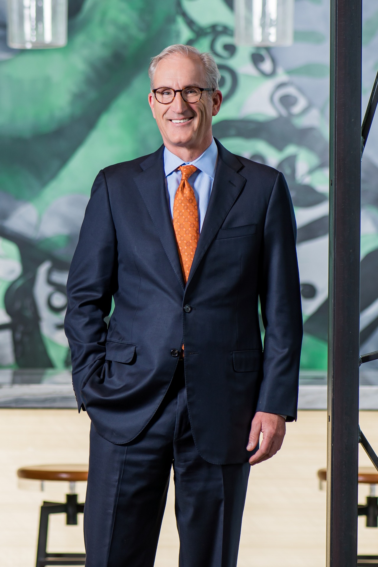 Mike Schlegel stands confidently in a suit against a colorful abstract mural backdrop.