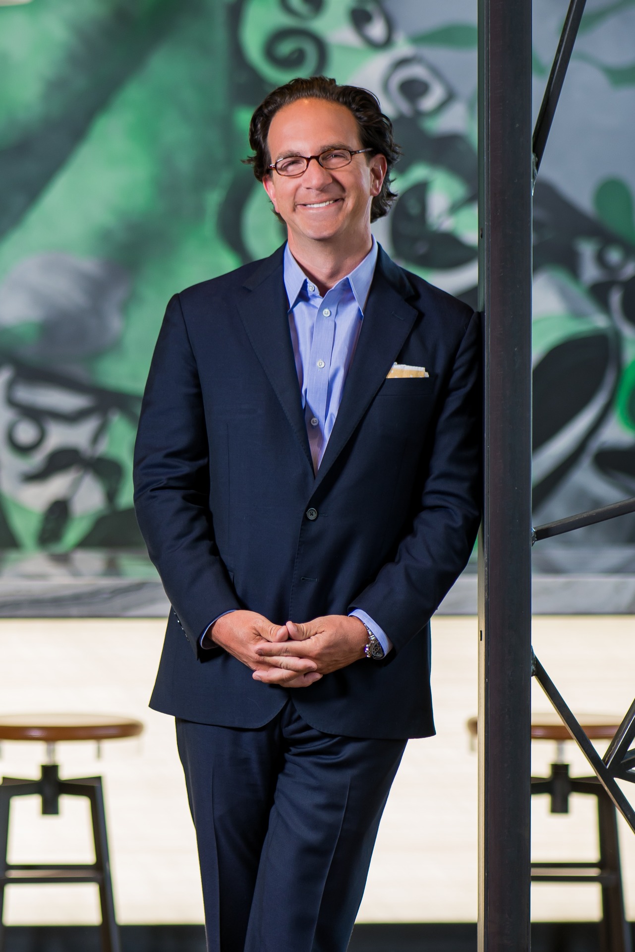 Toby Bozzuto stands smiling in a stylish suit against a colorful background.