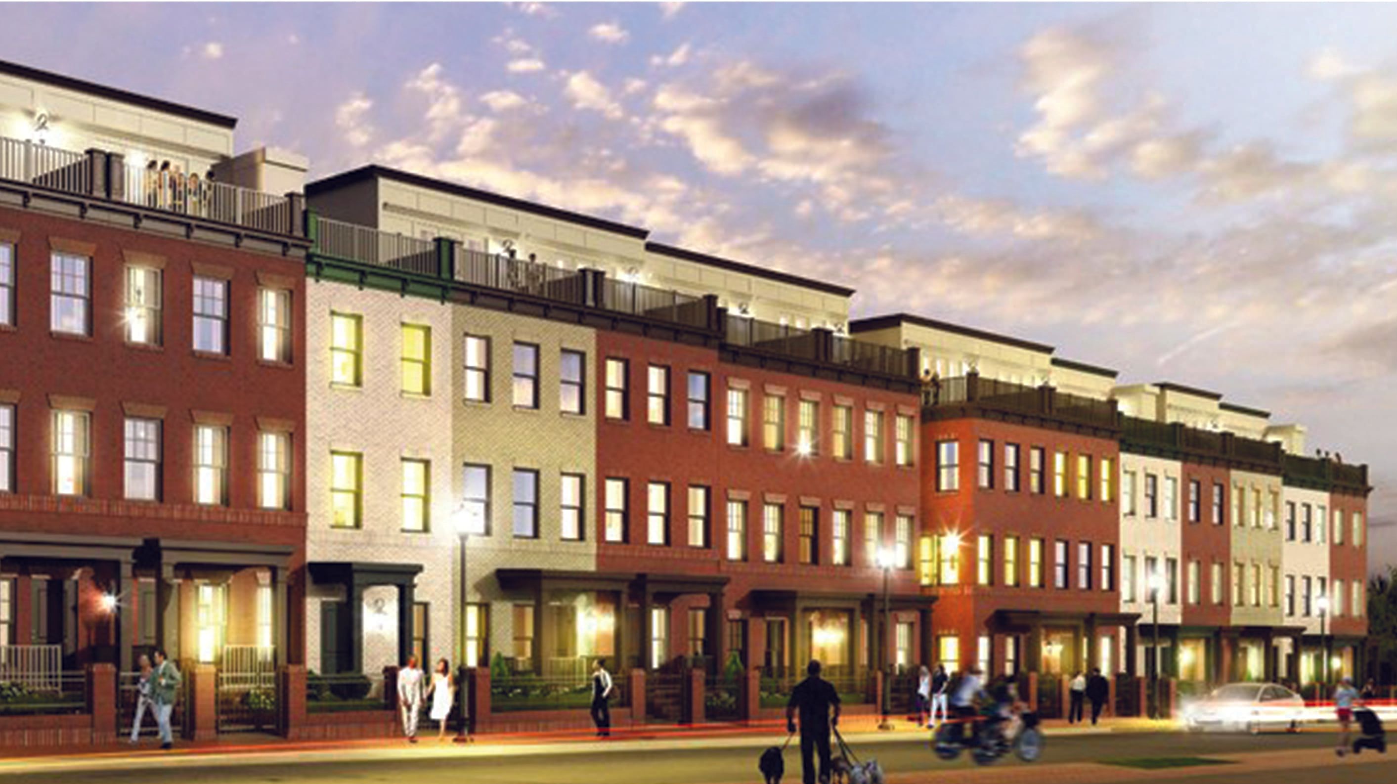 Modern townhouses lined up at dusk with people walking and decorative lighting.