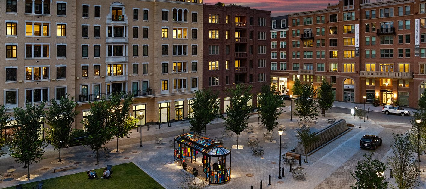 Modern apartment buildings surround a pedestrian plaza at dusk.